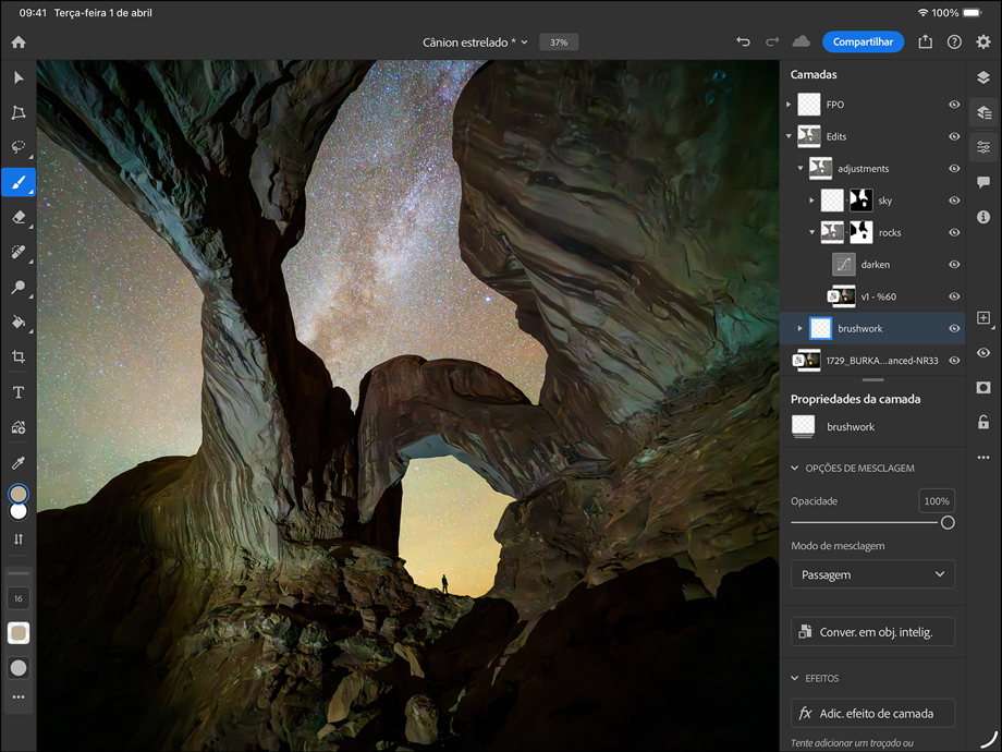 Parte da frente do iPad Pro preto-espacial na horizontal, tela com borda preta, cantos arredondados, mostrando a edição de uma fotografia de um desfiladeiro e um céu estrelado. À direita, camadas, ferramentas e efeitos visíveis, incluindo pinceladas, ajustes e outros