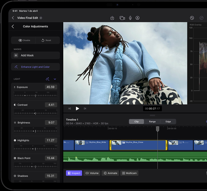 iPad Pro, parte delantera exterior, bisel de pantalla negro, la pantalla muestra una aplicación de edición de vídeo con una imagen de una modelo con abrigo azul y pantalones estampados en blanco y negro, panel de ajuste de color abierto a la izquierda con varios reguladores y efectos de vídeo, línea de tiempo en la parte inferior con varios clips de vídeo y pistas de audio