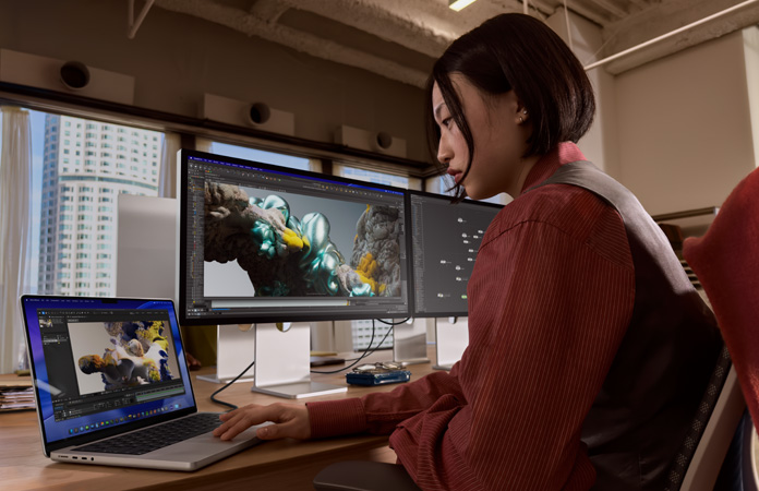 A person working in an office setting with MacBook Pro connected to Studio Display XDR